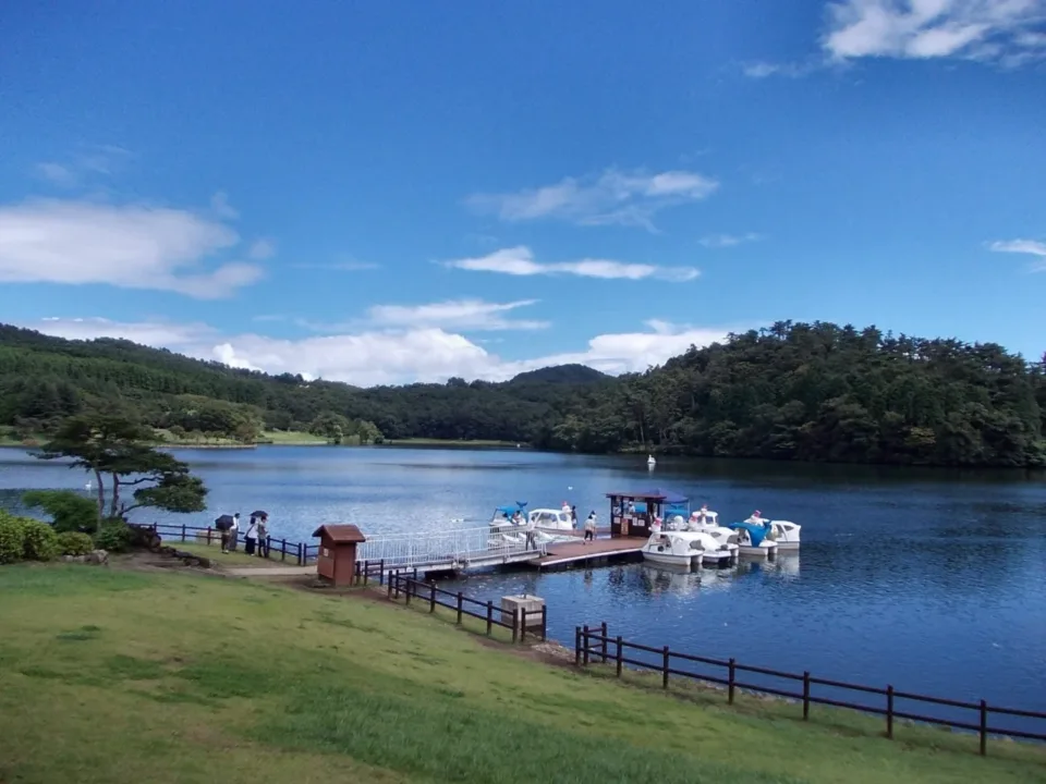 別府志高湖湖畔景色,湖面停泊著小船,後方是綠意盎然的山丘
